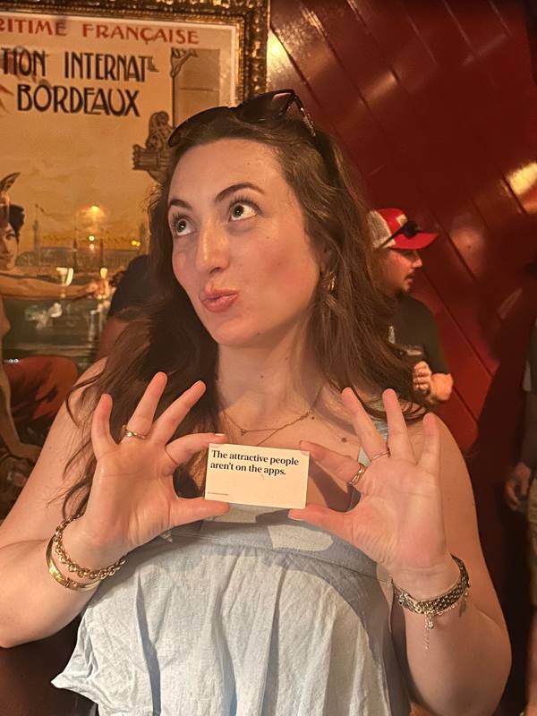 An ambassador holding a No.Regrets card that reads 'The attractive people aren't on the apps.'